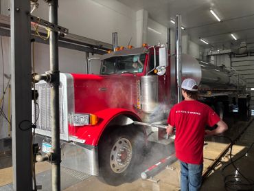 Worker washing commercial truck with high pressure spray